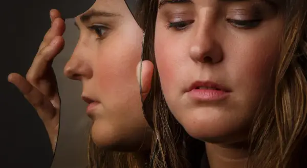 Ragazza con volto riflesso in uno specchio rotto, un'immagine che evoca cosa fa arrabbiare un bipolare.