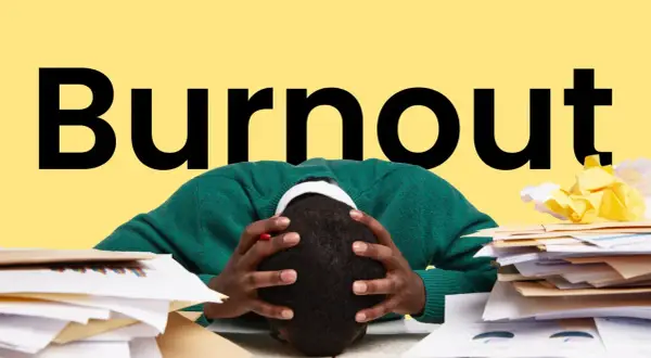 Persona con la testa tra le mani, circondata da pile di documenti, con la parola "Burnout" in grande sullo sfondo giallo. Sintomi di esaurimento.