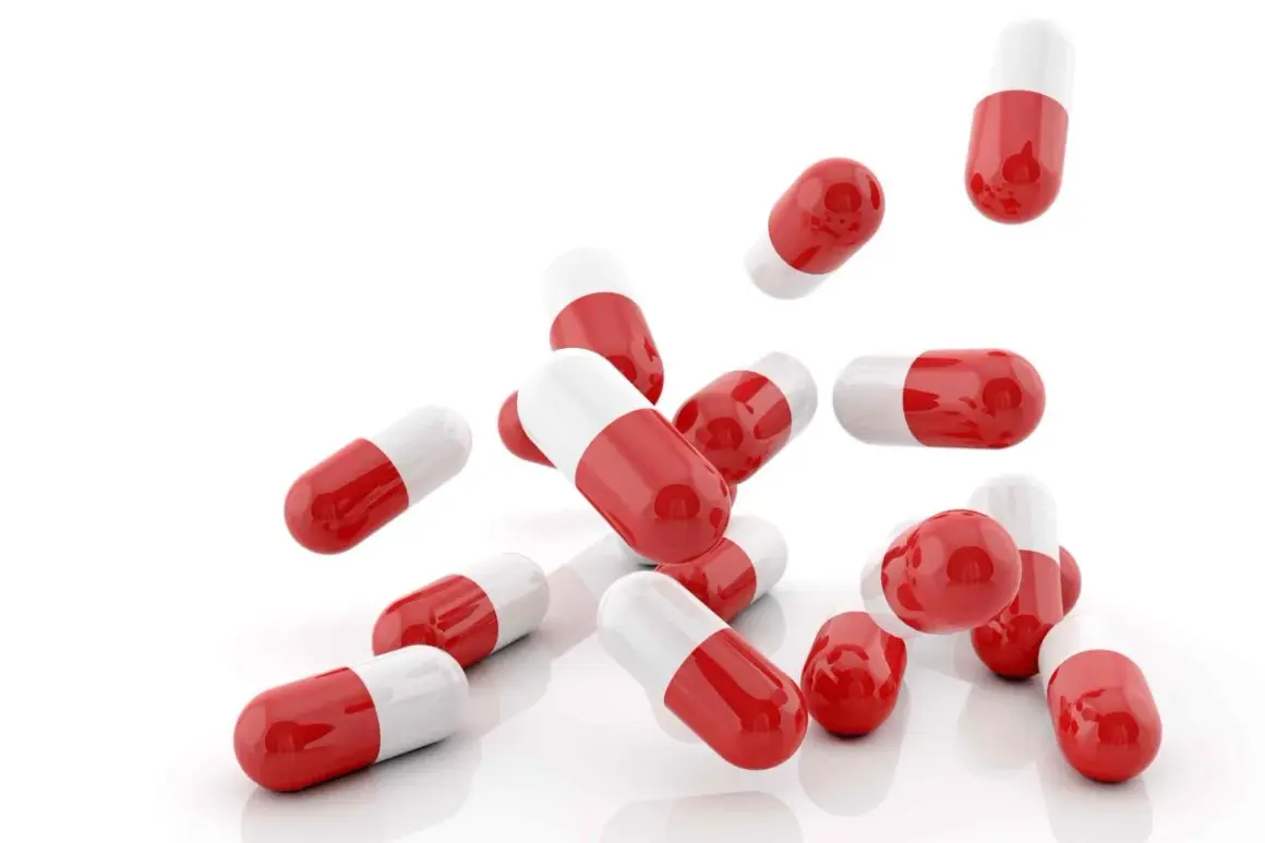 Capsule rosse e bianche, utili come cortisone per mal di gola, sparse su sfondo bianco.