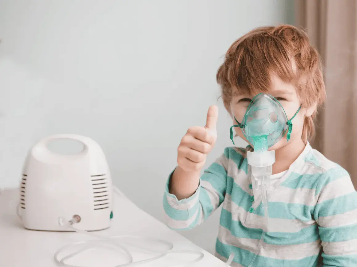 Bambino con maschera per aerosol, pollice in su. L'aerosol è pronto, prima o dopo i pasti, per respirare meglio.