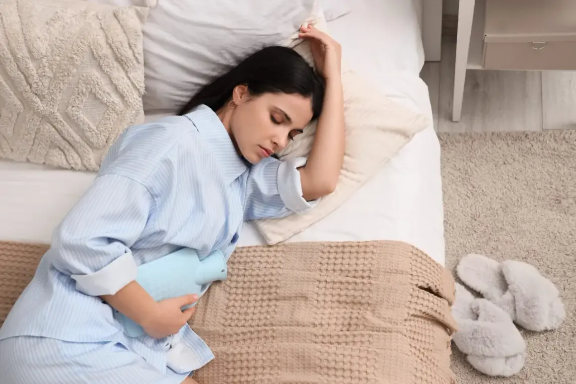 Donna a letto con una borsa dell'acqua calda sull'addome, cercando sollievo. Un'immagine che evoca il desiderio di sapere come far venire il ciclo.