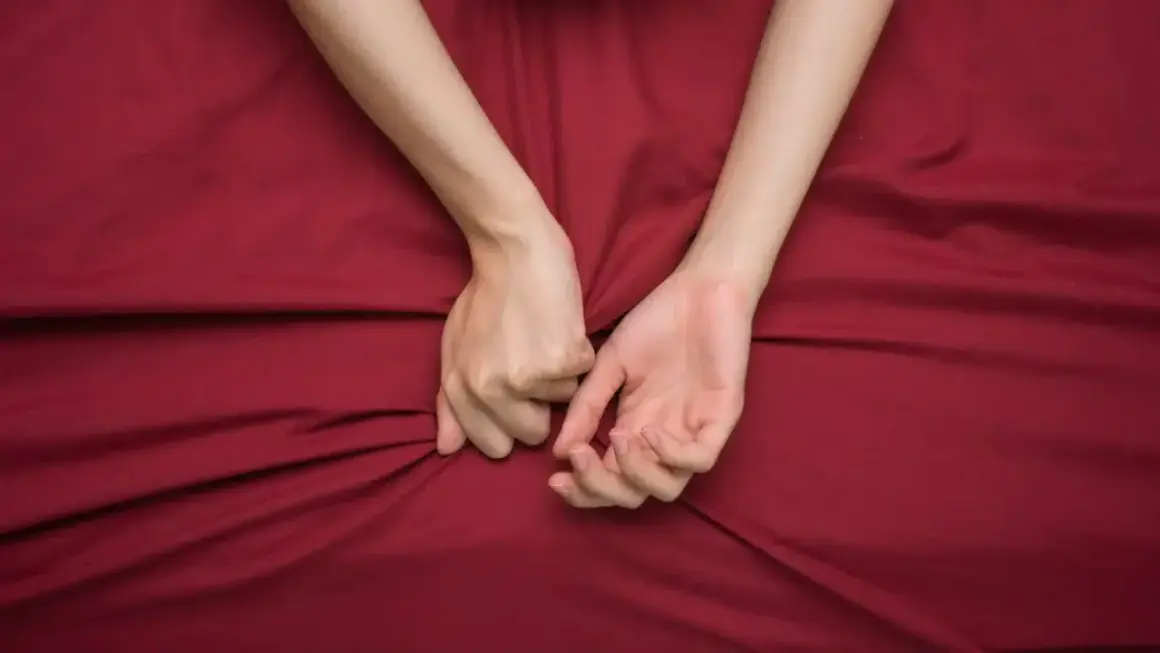 Mani intrecciate su lenzuola rosse, un simbolo di passione intensa, a volte legata al disturbo bipolare e all'ipersessualità.