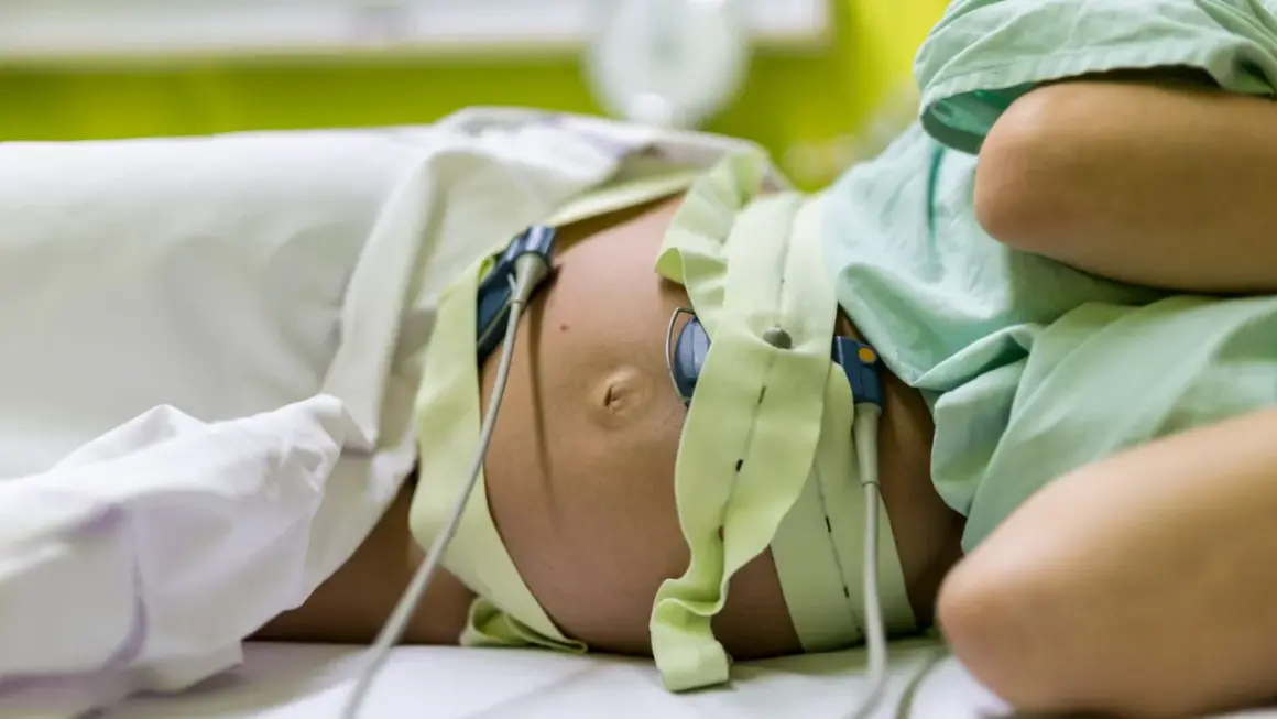 Pancia di donna incinta con monitoraggio per il parto indotto. Le fasce verdi e i sensori sono posizionati per monitorare il battito cardiaco del feto.