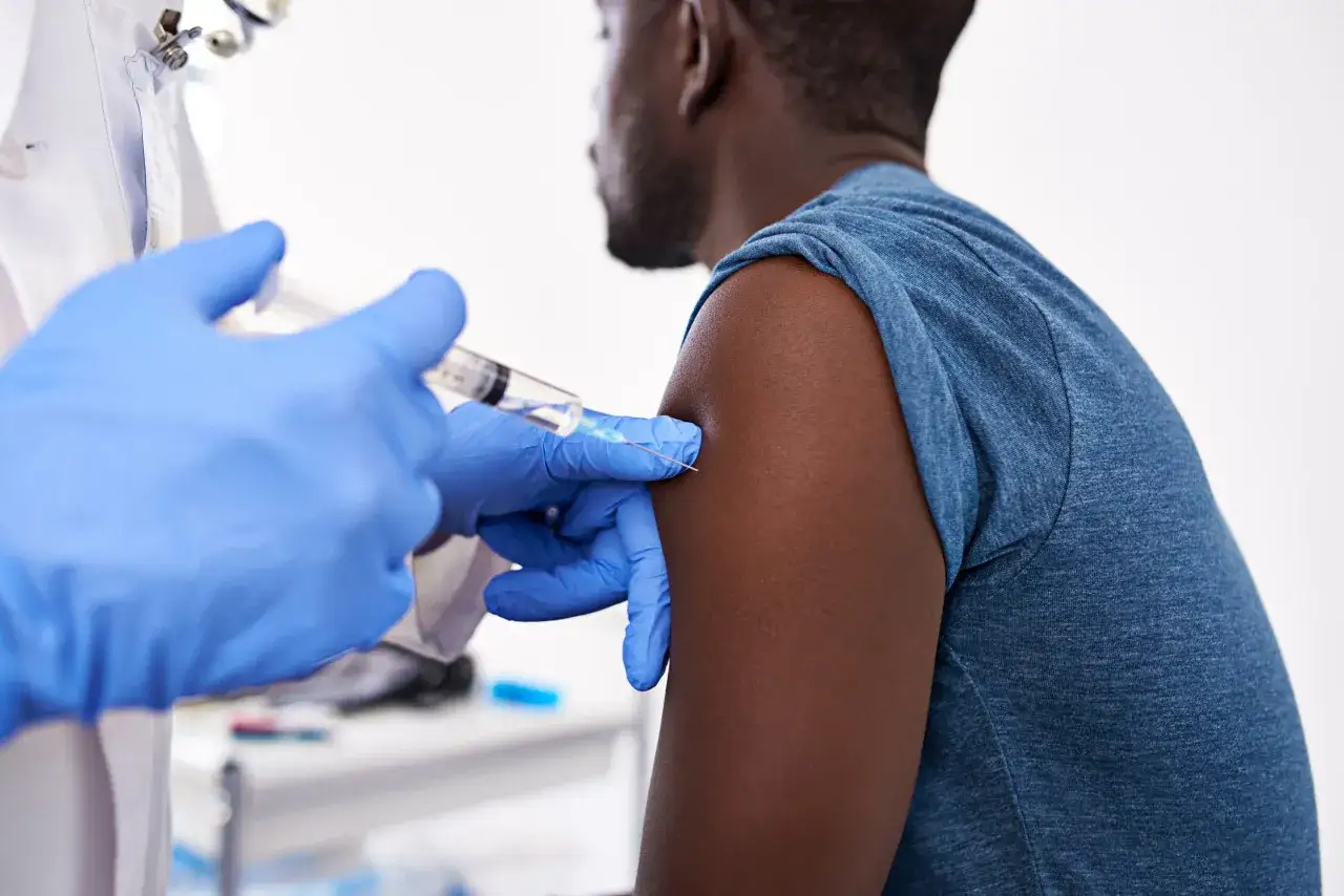 Un medico con guanti blu somministra un vaccino herpes zoster. Si discute dei possibili effetti collaterali.