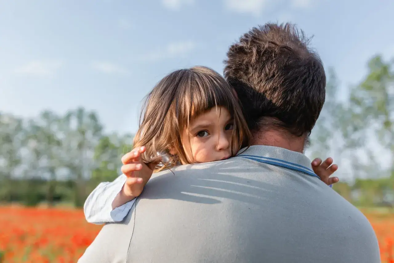 Bambina abbracciata al padre in un campo di papaveri. La sua espressione trasmette un profondo significato psicologico di sicurezza e amore, una vera carezza per l'anima.