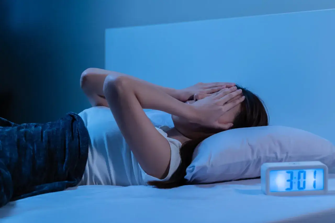 Donna a letto, con le mani sugli occhi, soffre di ansia notturna. L'orologio digitale segna le 3:01.