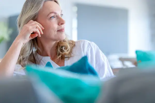 Donna bionda con mano sul viso, pensierosa. Si interroga a che età si va in menopausa, un momento di transizione.