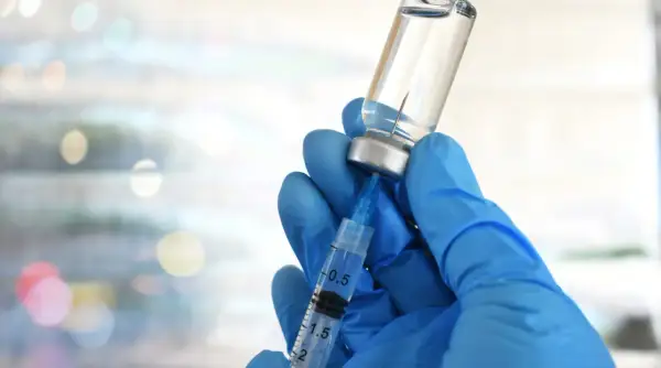Mano guantata blu aspira liquido da fiala. Preparazione vaccino herpes zoster, attenzione agli effetti collaterali.