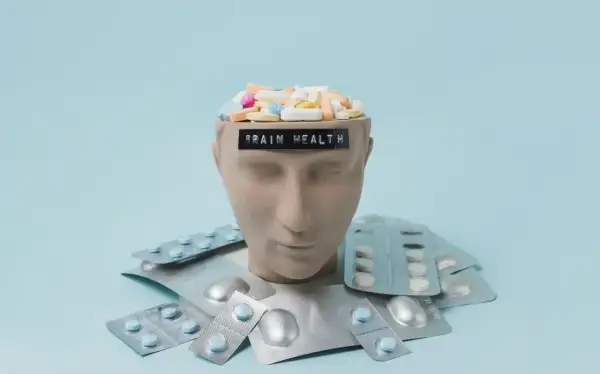 Testa di manichino piena di pillole, con blister intorno. La scritta "BRAIN HEALTH" suggerisce che gli psicofarmaci danneggiano il cervello.