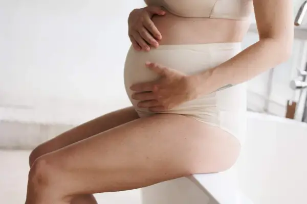 Donna incinta con mani sul pancione, che affronta la stitichezza in gravidanza.