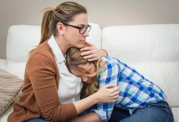 Madre abbraccia figlia in lacrime, offrendo conforto. Un gesto d'amore che può aiutare a superare le cause dell'anoressia.