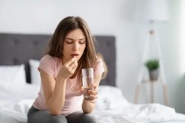 Donna con un bicchiere d'acqua e una pastiglia, forse Efferalgan 1000, per alleviare un malessere.