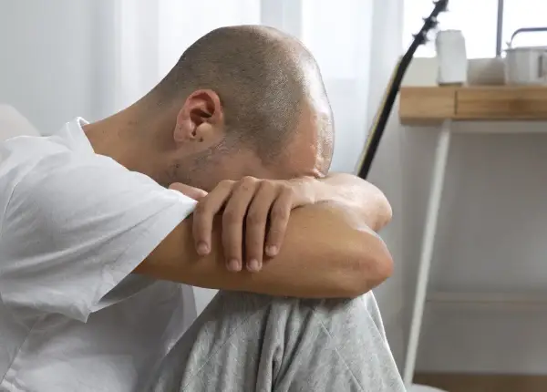 Uomo con la testa tra le braccia, in un momento di profonda riflessione e elaborazione del lutto.