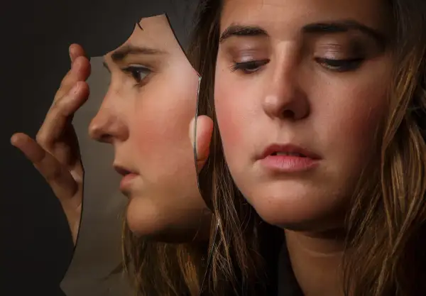Ragazza con volto riflesso in uno specchio rotto, un'immagine che evoca cosa fa arrabbiare un bipolare.