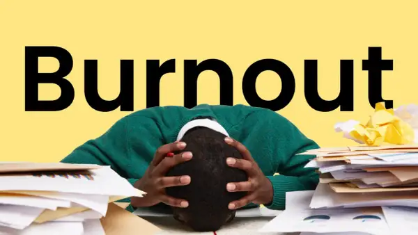 Persona con la testa tra le mani, circondata da pile di documenti, con la parola "Burnout" in grande sullo sfondo giallo. Sintomi di esaurimento.