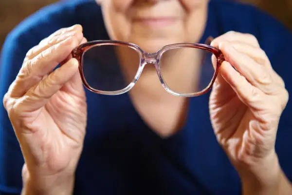Mani anziane tengono occhiali. Domanda: quanto tempo aspettare per fare occhiali dopo intervento cataratta?